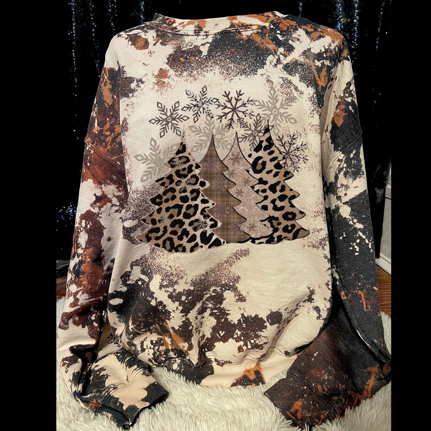 Sweater with snowflake, tree, and leopard print design on a black background