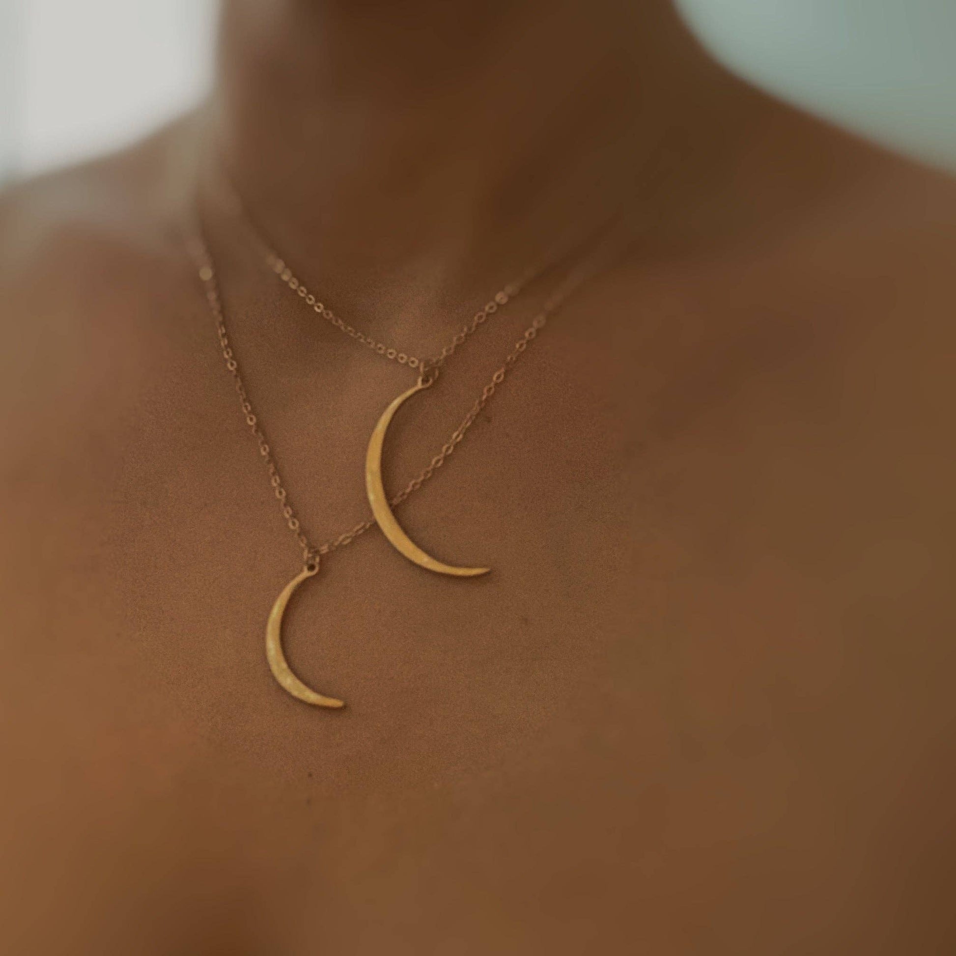 Gold crescent moon necklace on a person's neck with a blurred background