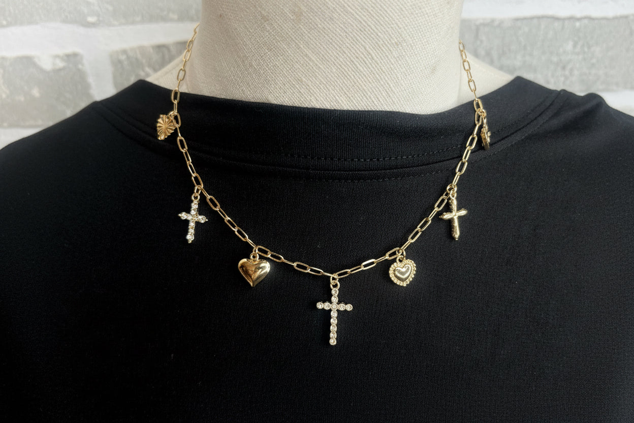 A gold charm necklace with hearts and crosses on a black shirt