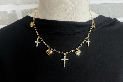 A gold charm necklace with hearts and crosses on a black shirt