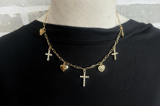 A gold charm necklace with hearts and crosses on a black shirt