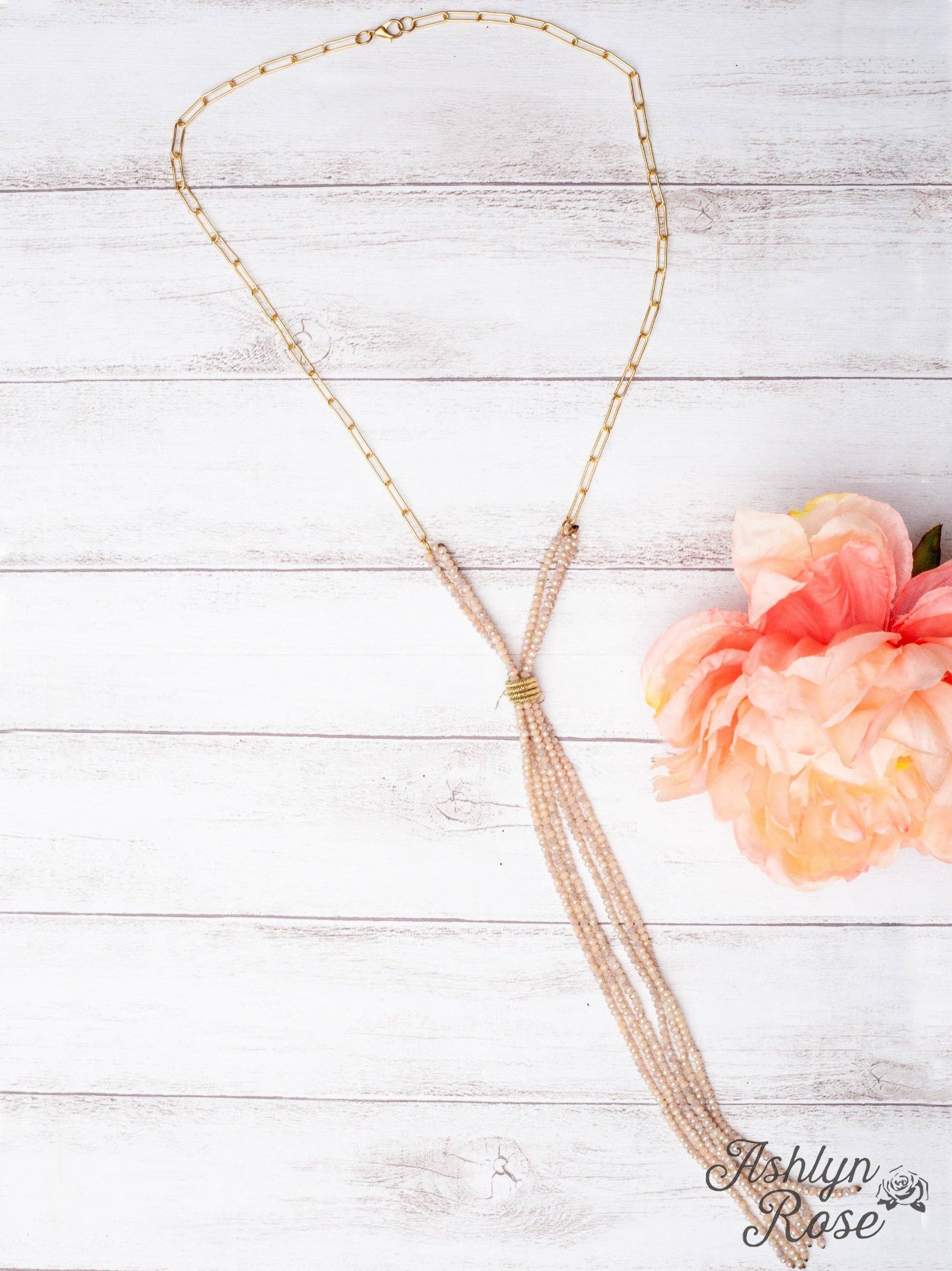 Gold  beaded necklace on a light wooden surface with a pink flower