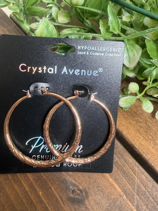 Gold hoop textured earrings on a jewelry card on a board with greenery