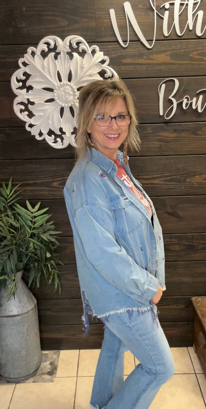 Woman wearing a denim jacket and jeans standing in front of a decorative wall with text.