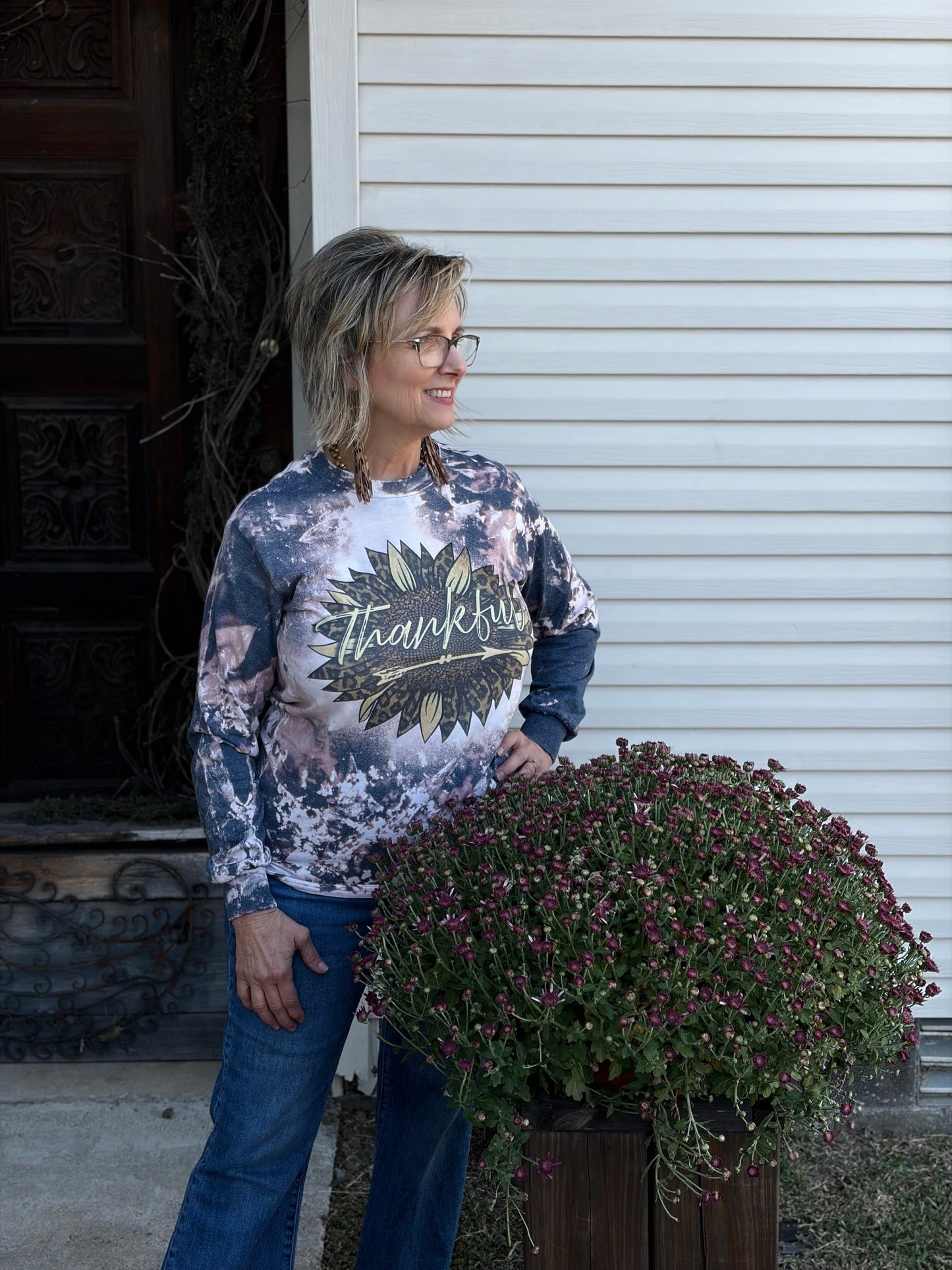 Woman wearing a 'Thankful' shirt in front of a large potted plant.