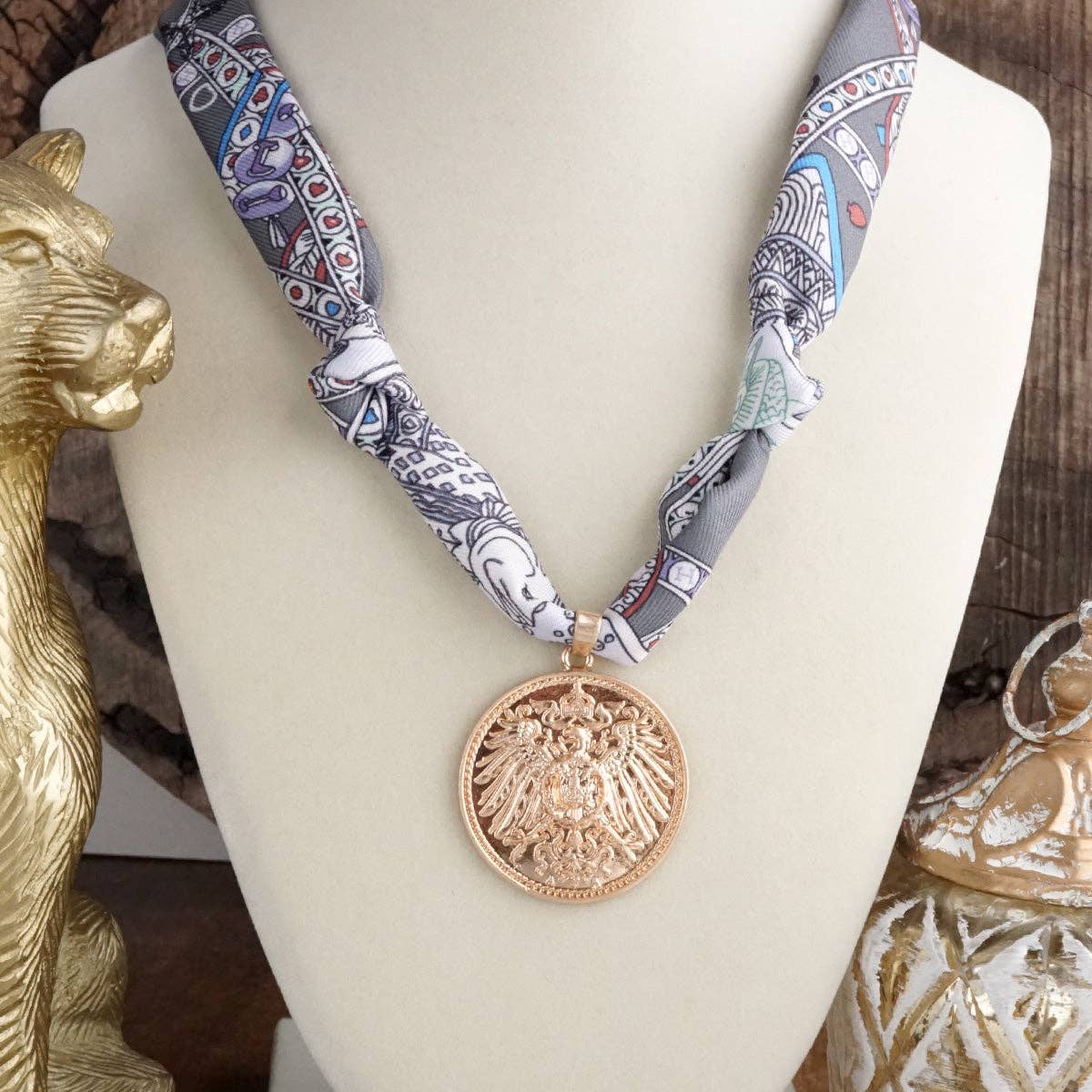 Decorative eagle coin necklace on a grey printed scarf shown on a bust