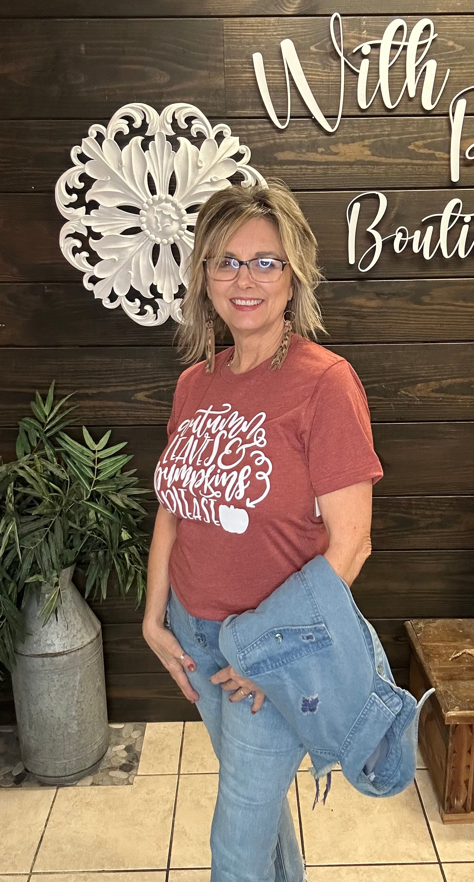 Woman wearing a rust t-shirt with text and graphics, standing in front of a decorative wall.
