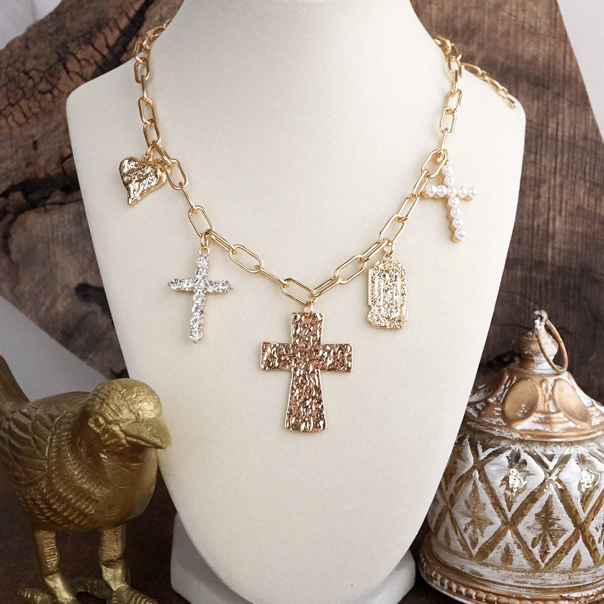 Gold necklace with various pendants on a white mannequin bust against a rustic background.