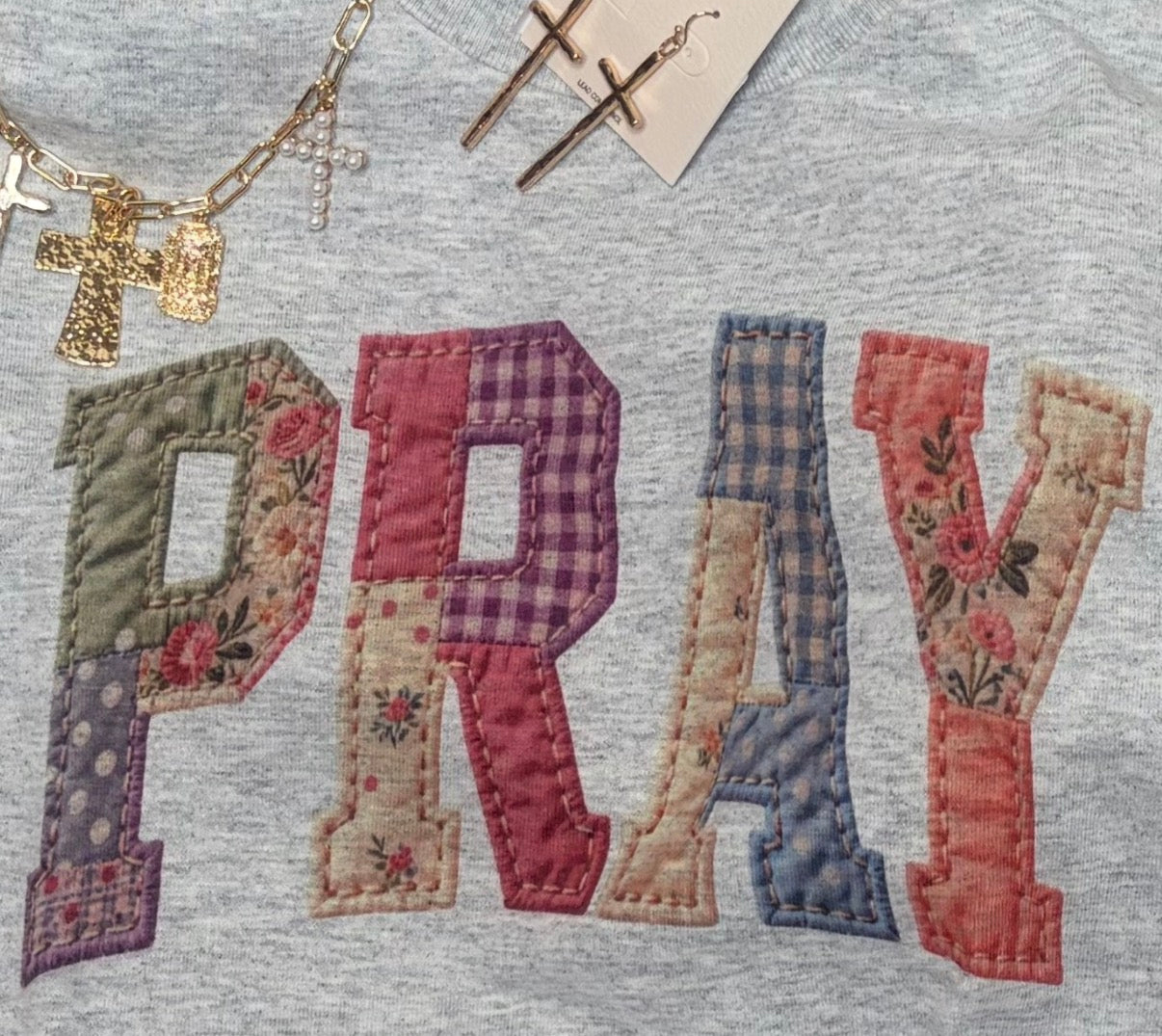 the look of quilted letters spelling 'PRAY' on a gray fabric background with religious accessories.