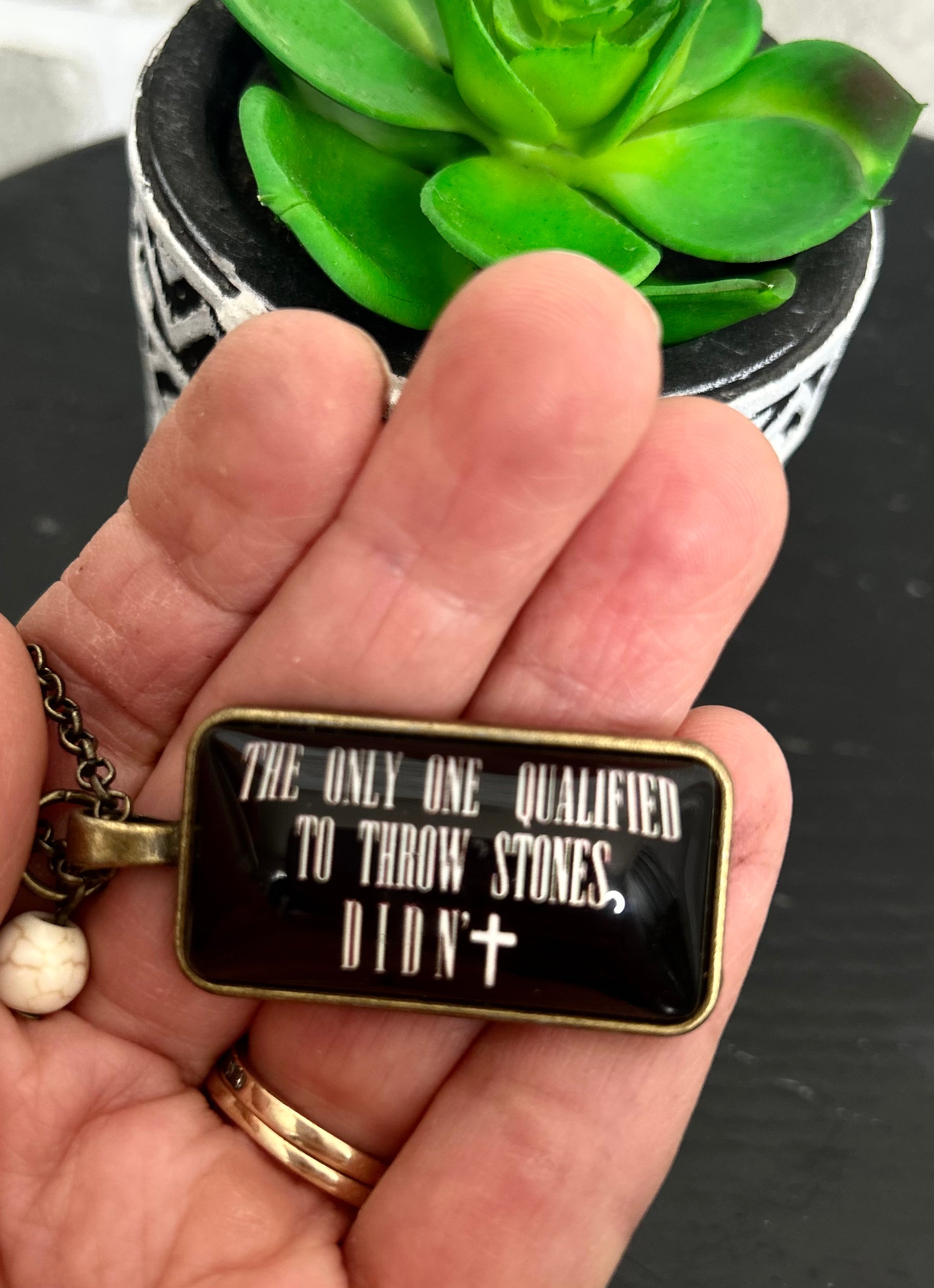 long chain necklace with glass rectangle pendant with "The Only One qualified to throw stones didn't" message, adorned with a small white bead.