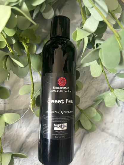 Bottle of Sweet Pea Goat Milk Lotionon a surface with green leaves in the foreground