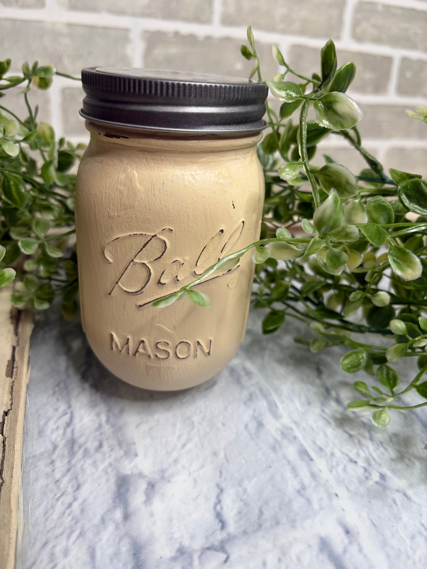 soft  yellow mason jar with a rustic lid against a light gray background with greenery.