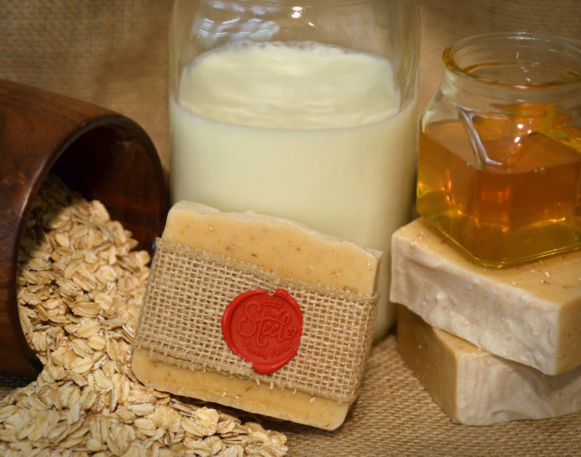 Bar of soap with a red wax seal, jar of milk, and jar of honey on a textured surface.