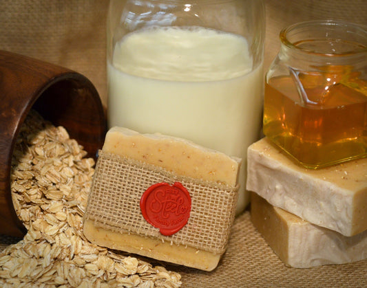 Bar of soap with a red wax seal, jar of milk, and jar of honey on a textured surface.