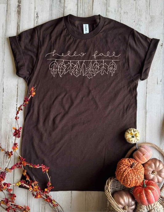 Chocolate colored tee with outline of fall leaves & hello fall graphic shown with pumpkins 