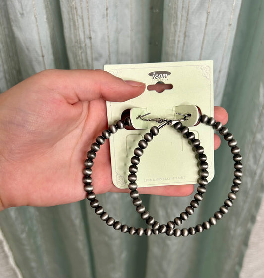 Hand holding a beaded earrings on a 'icon' branded card against a neutral background
