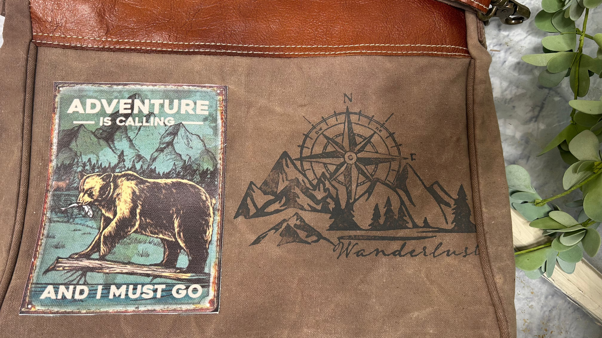 Immerse yourself in the thrill of the unknown with the Adventure Is Calling And I Must go. Zipper Closure Shoulder Bag, featuring a bear &amp; fish wilderness scene...compass and mountain range! Unique, Quality, + Character....

Measuring at 14" x 12.5" x 1.5", this bag is perfect for the woman on the go. It's not just a bag, but a statement piece that brings out your adventurous spirit. Crafted from repurposed tent and canvas, it embodies sustainability while maintaining a stylish appeal.

Inside zip pocke