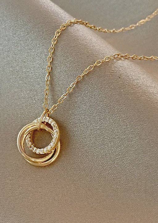 Gold necklace with interlocking rings on a beige fabric background