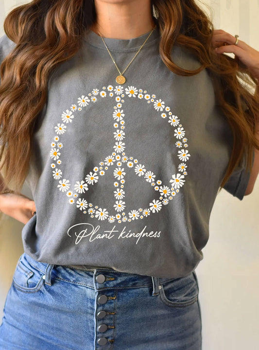 person wearing a gray tee shirt with a peace symbol made from yellow and white daisy's that says plant kindness