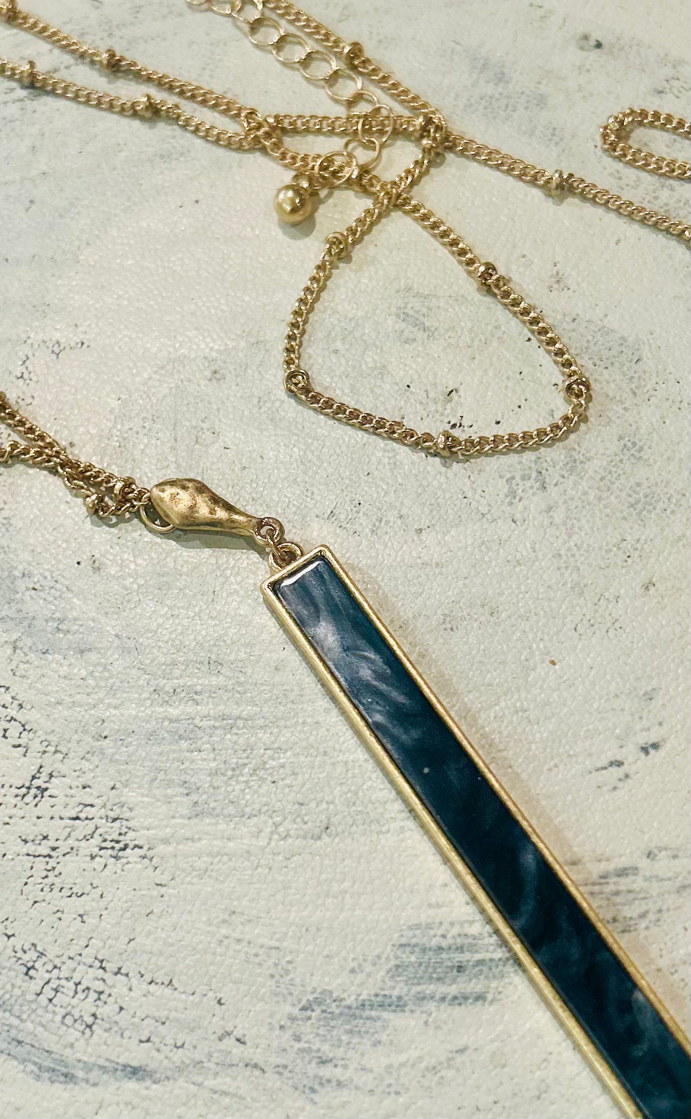 Gold necklace with a black bar pendant on a textured surface