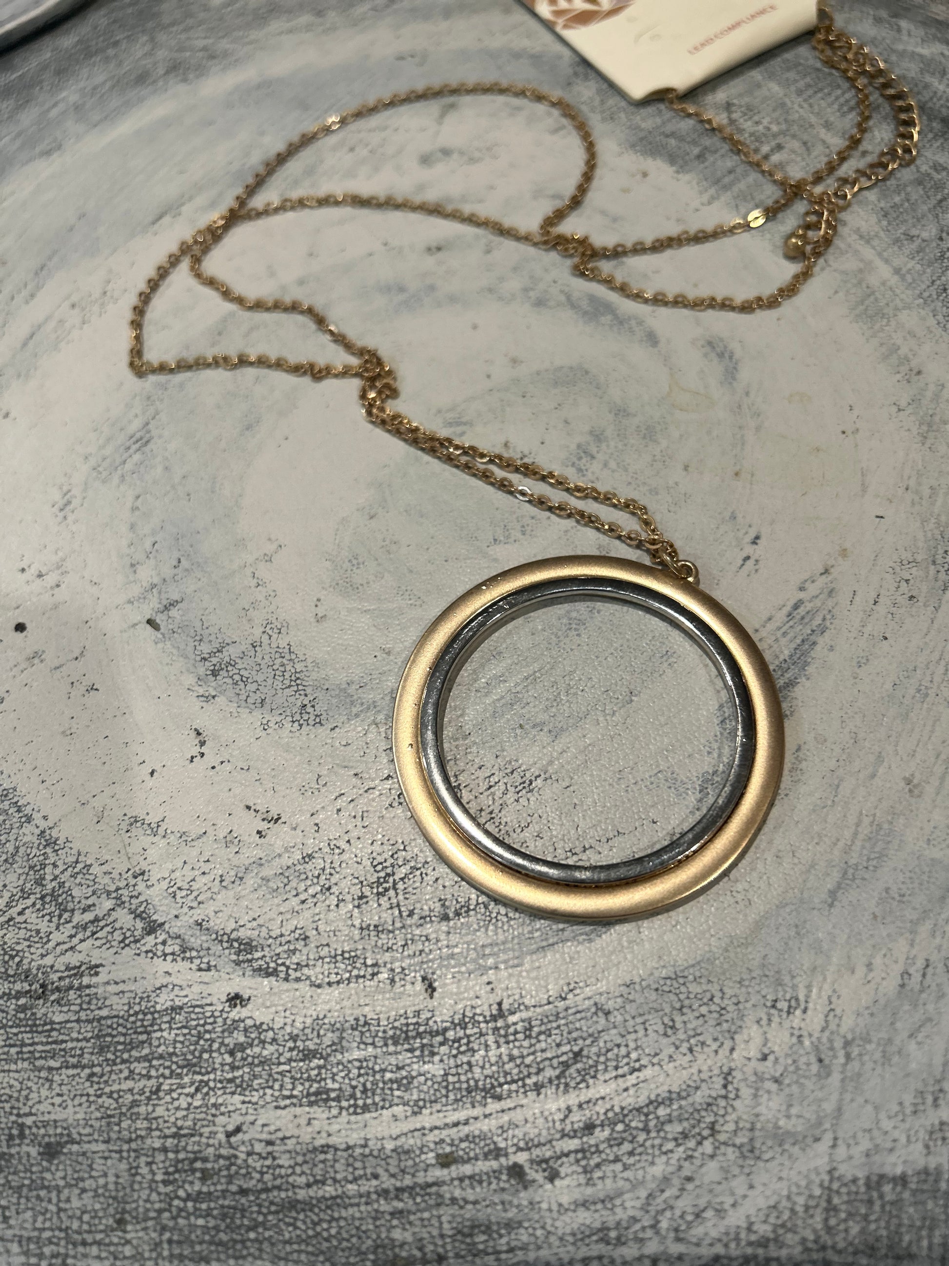 Gold necklace with a round pendant of gold and silver on a textured gray surface