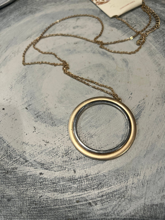 Gold necklace with a round pendant of gold and silver on a textured gray surface