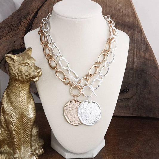 Necklace with chain and round pendants on a mannequin bust, next to a gold cat figurine.