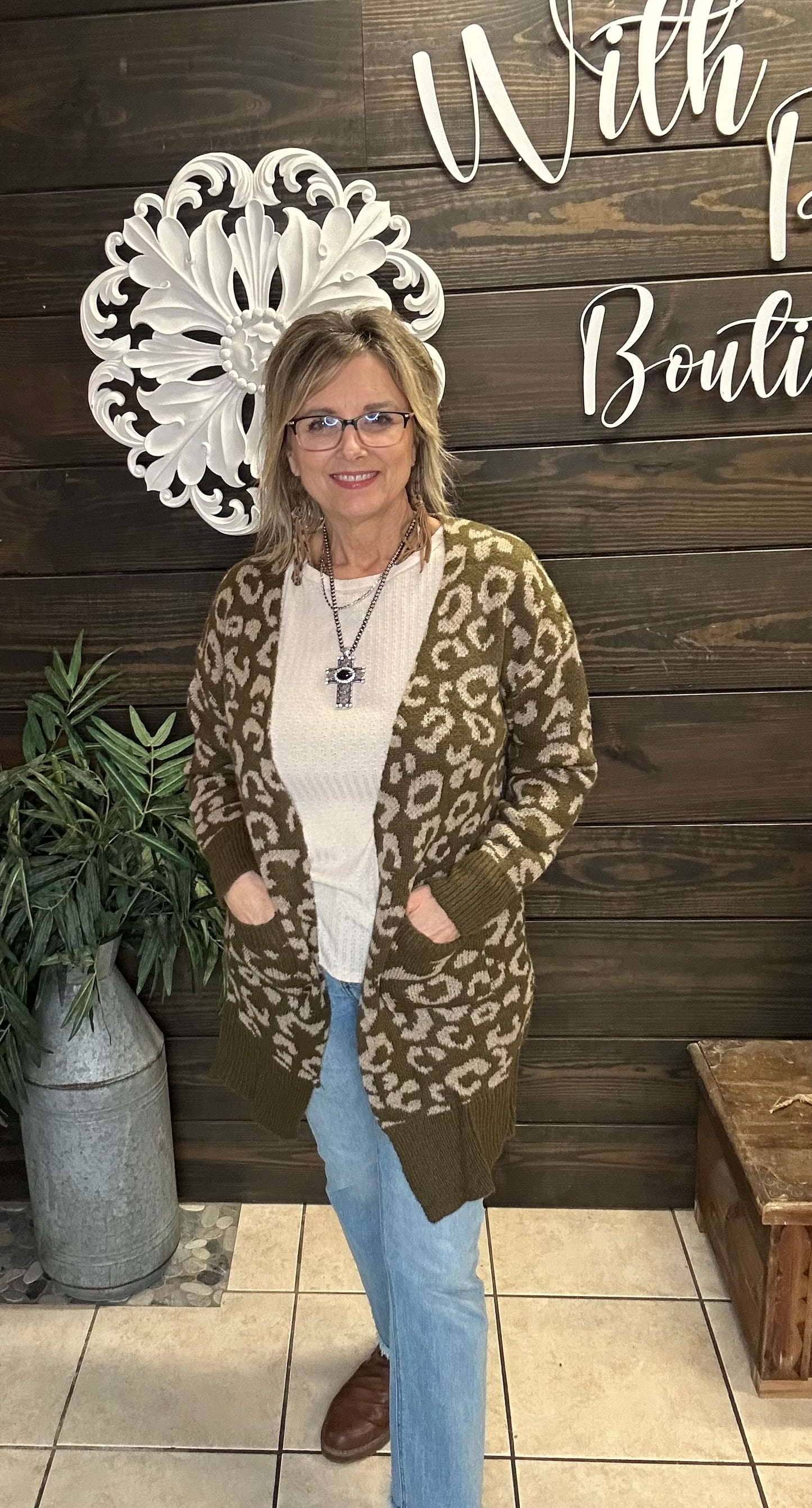Woman wearing a olive leopard print cardigan in front of a wooden wall with decorative elements.