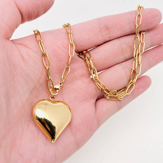 Gold heart-shaped pendant necklace on a hand with a white background