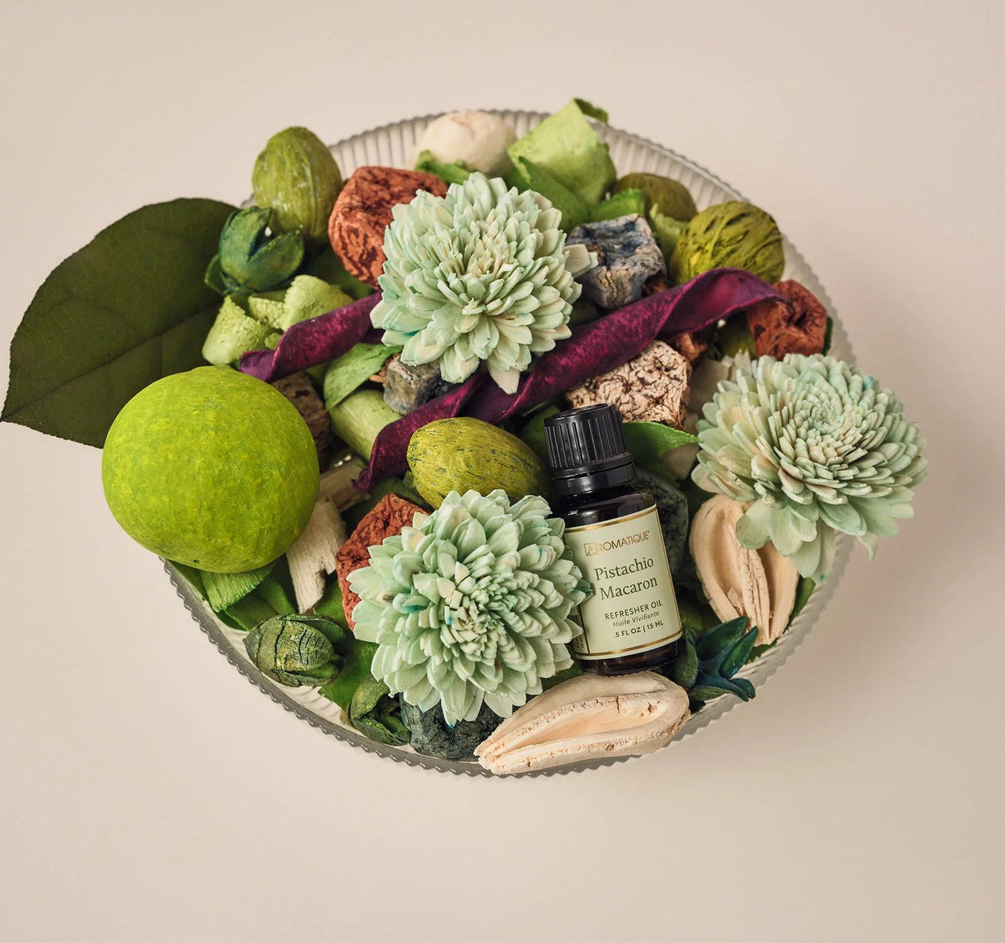 Decorative arrangement with green flowers, leaves, and a small bottle on a beige background