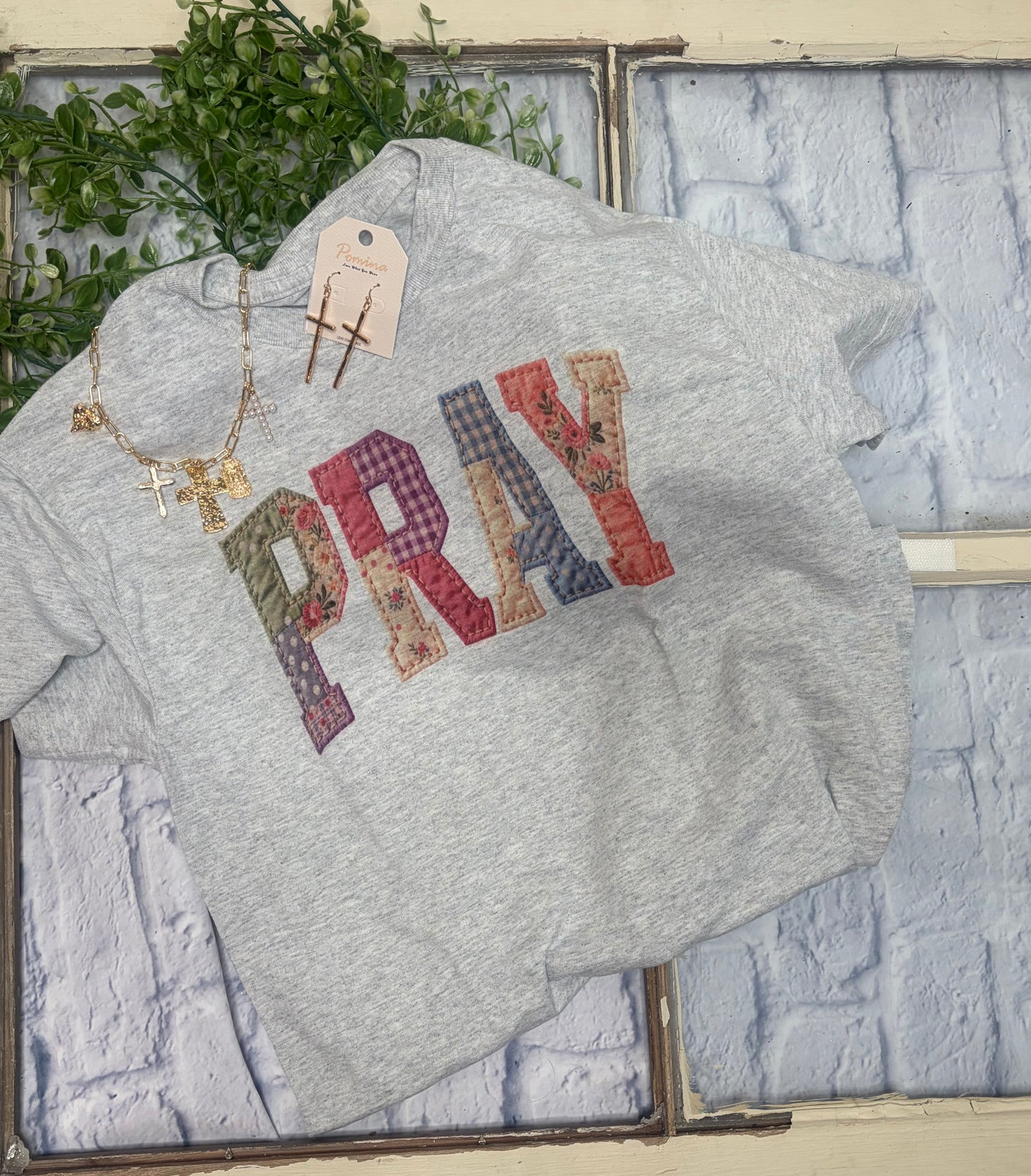 Gray tee shirt with 'PRAY' text in colorful patches on a textured wall back ground 