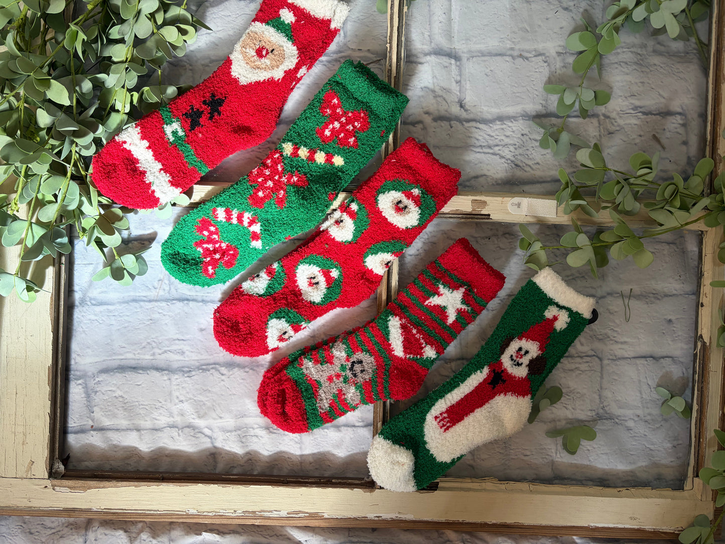 Set of colorful knitted Christmas socks on a rustic wooden surface with greenery.