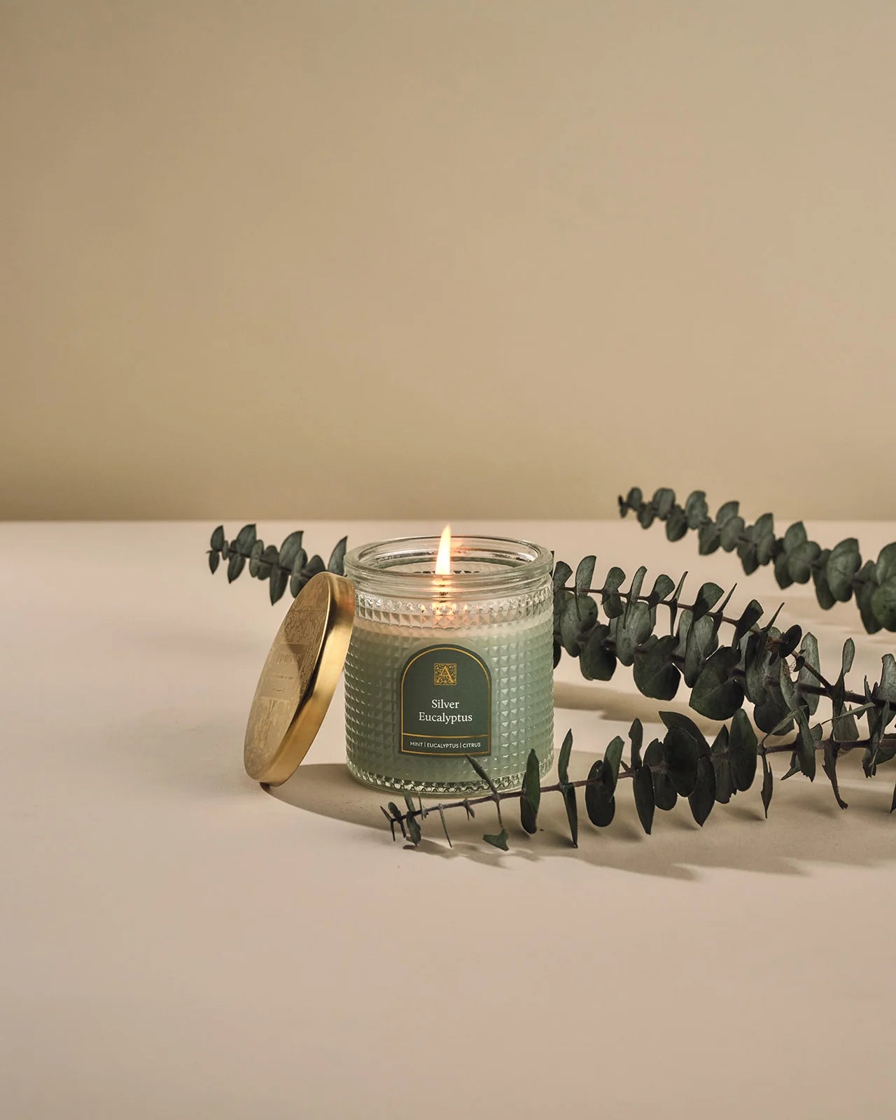 Candle with a green label and eucalyptus leaves on a beige background