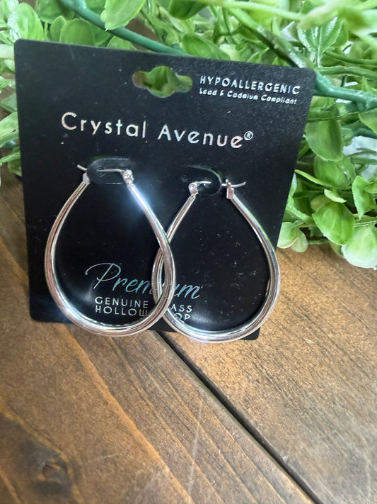 A pair of silver teardrop shaped earrings on a Crystal Avenue jewelry card placed on a wooden board with greenery