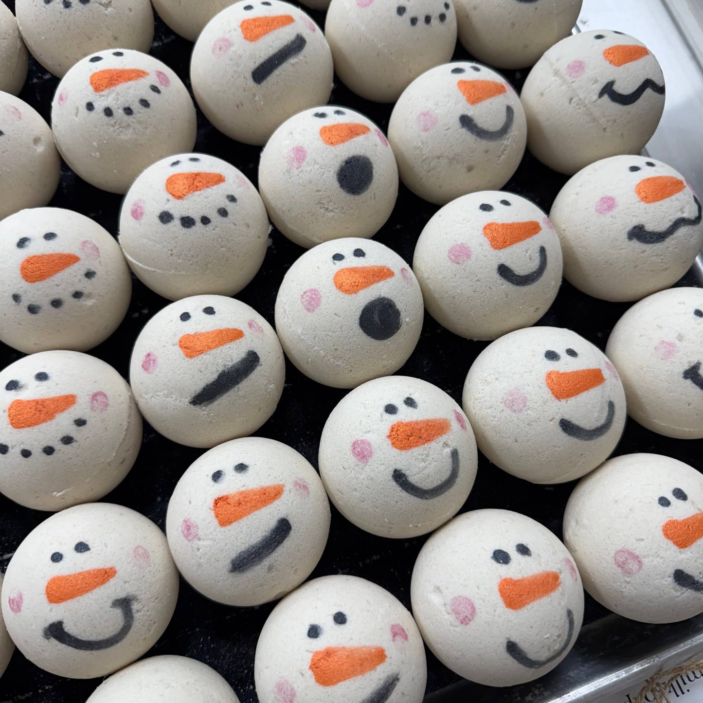 Bath bombs shaped like snowmen with orange carrot noses and black buttons on a tray.
