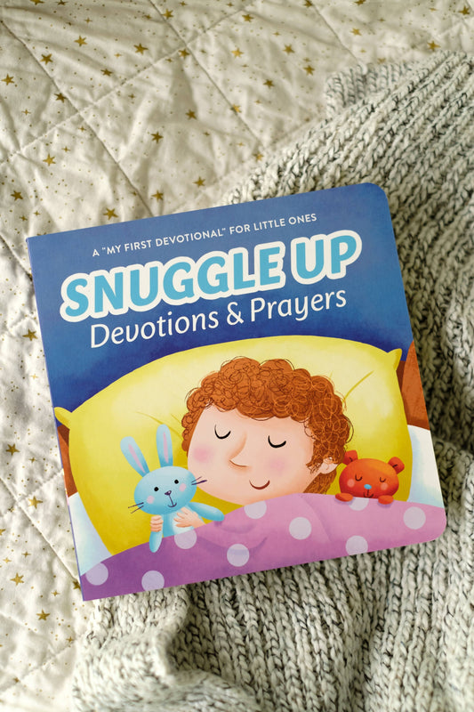 Book titled 'Snuggle Up Devotions & Prayers' for little ones on a textured fabric background