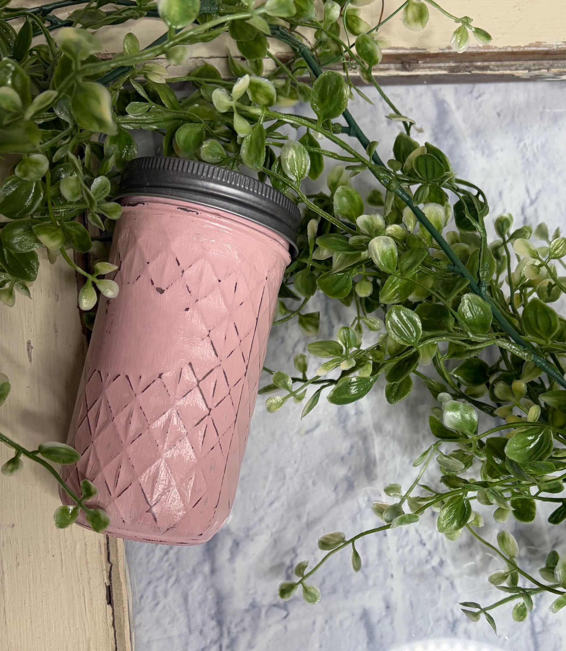 Pink textured tumbler with black lid on a white surface with green leaves