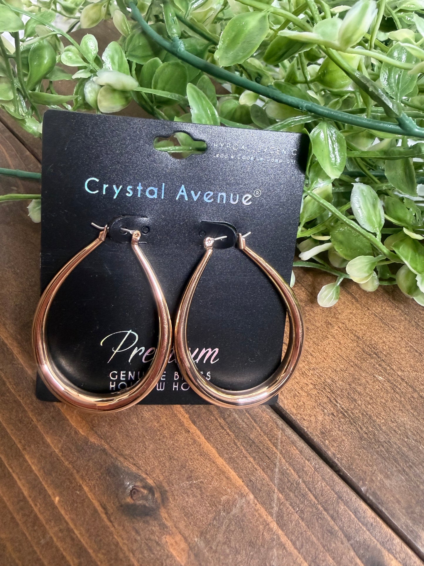 Gold teardrop earrings on a crystal avenue black card, on a wooden board with greenery