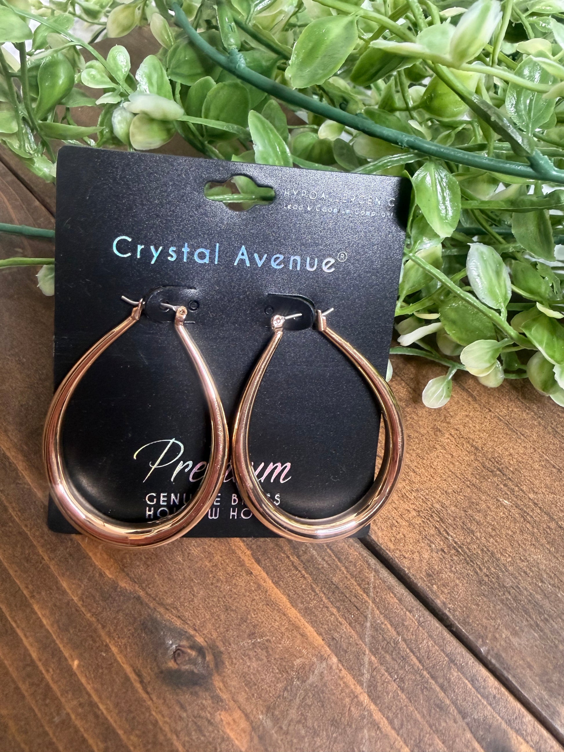 Gold teardrop earrings on a crystal avenue black card, on a wooden board with greenery