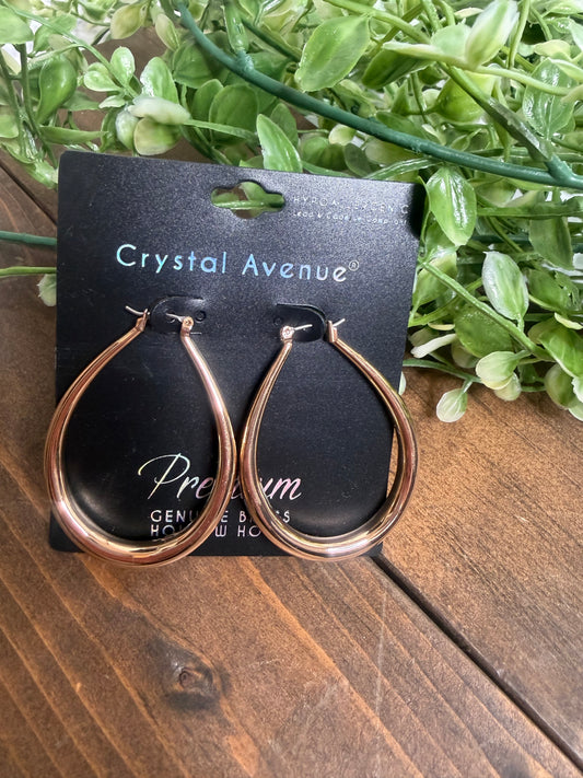 Gold teardrop earrings on a crystal avenue black card, on a wooden board with greenery