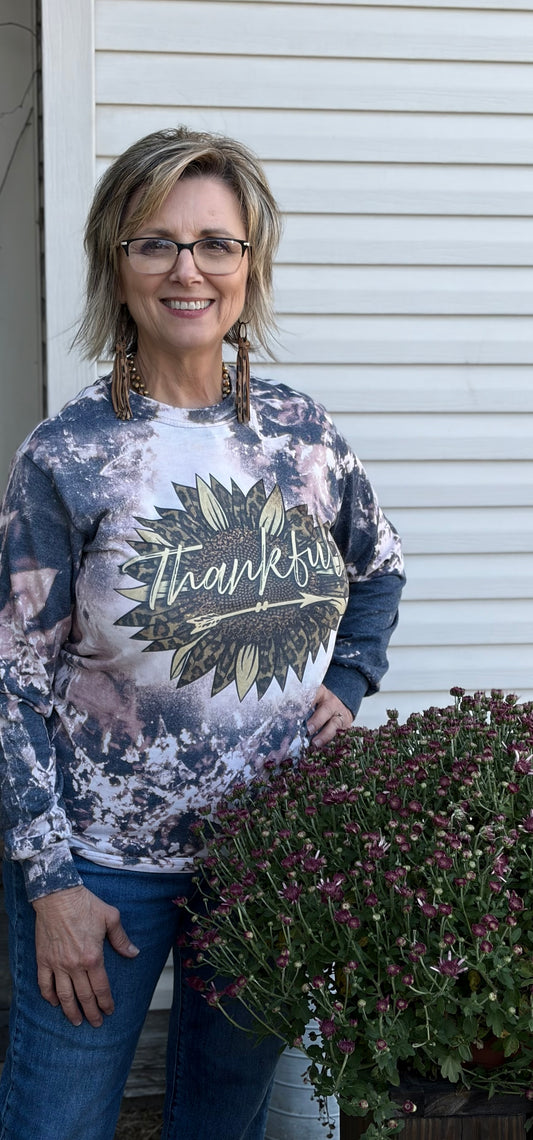 Woman wearing a 'Thankful' long sleeve tee standing in front of a white wall with plants.