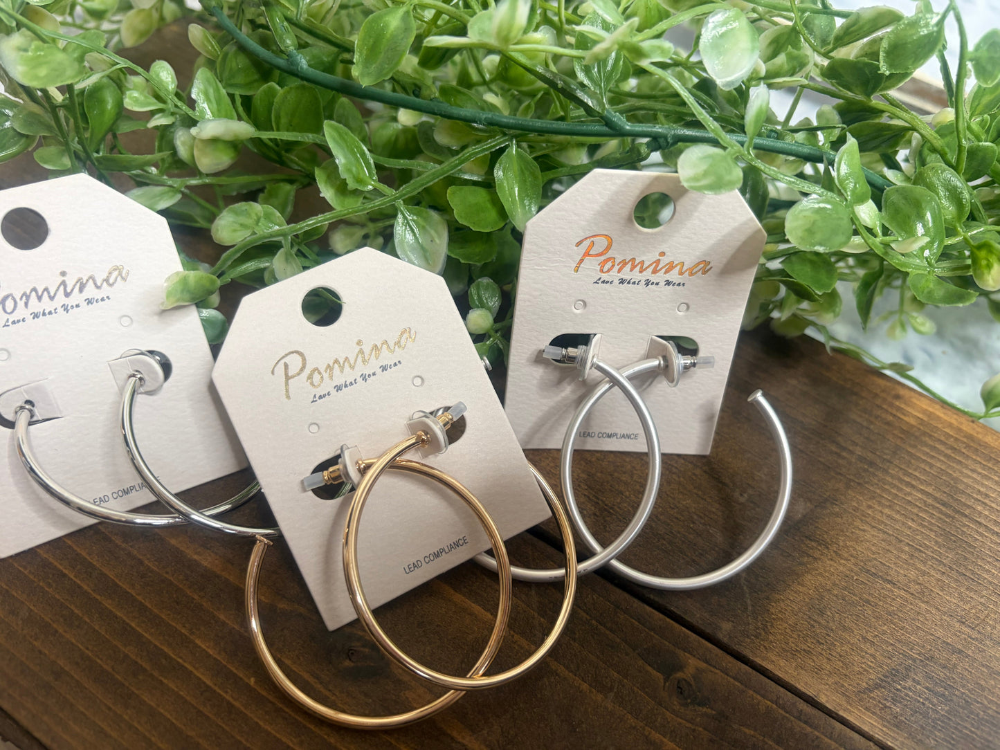 Three sets of hoop earrings one silver one matte silver one gold, on a w on a wooden background with greenery 