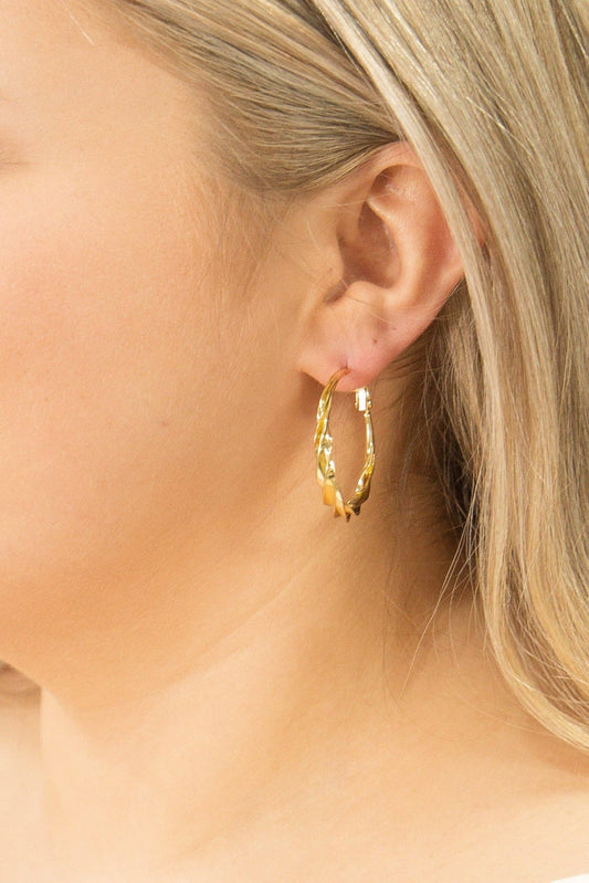 Close-up of a person wearing gold hoop earrings with a neutral background