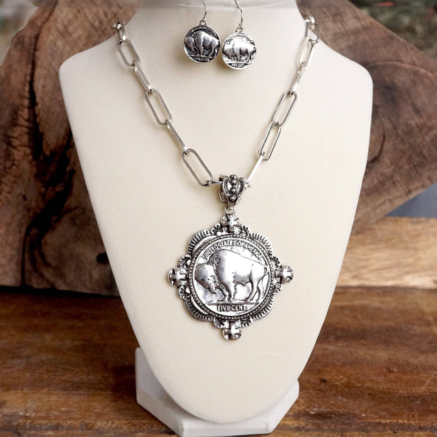 Silver necklace and earrings with buffalo design on a white stand against a wooden background