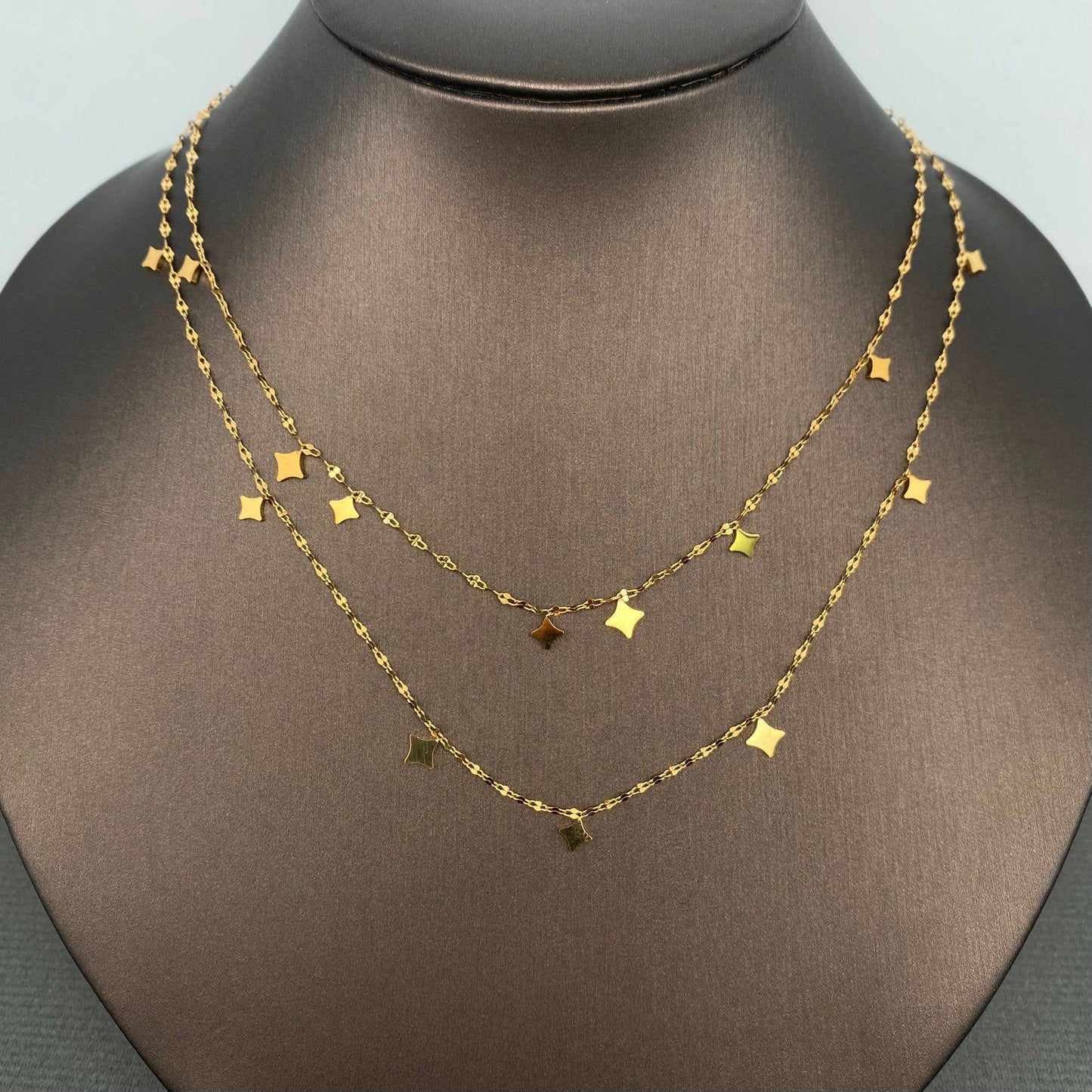 Gold necklace with star-shaped pendants on a mannequin bust.