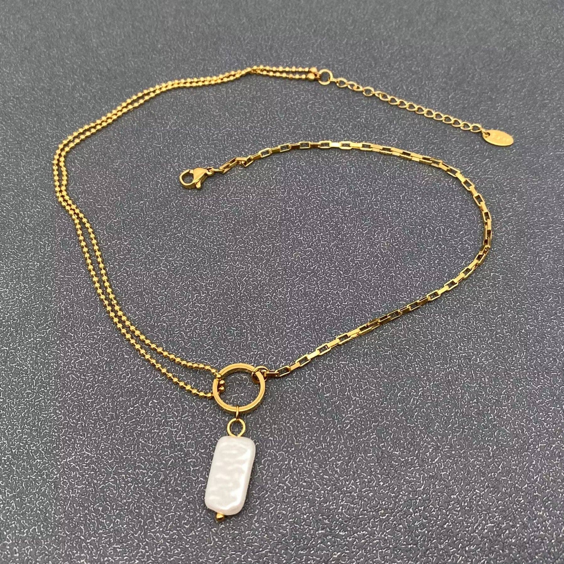 Gold chain necklace with a  pearl pendant on a gray background