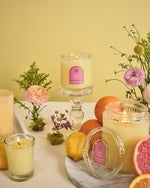 Candles with decorative labels on a table with fruits and flowers.