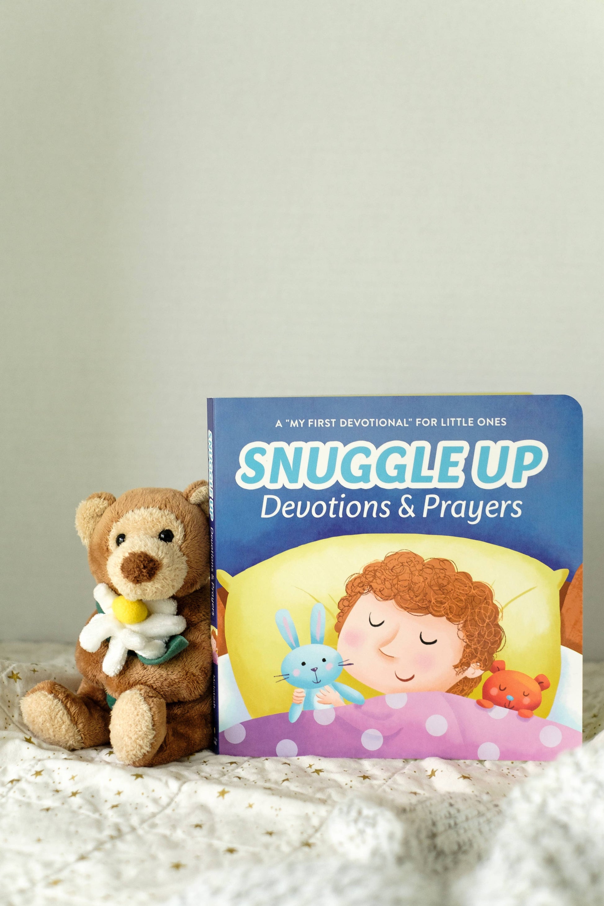 Children's book titled 'Snuggle Up Devotions & Prayers' with a teddy bear on a soft surface.