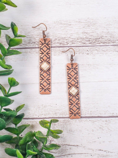 copper bar fishhook earrings with cream colored stone on a white board background with greenery