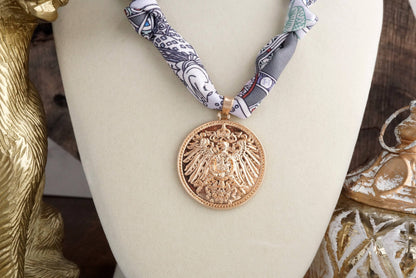 Gold pendant on a mannequin with a decorative scarf against a wooden background